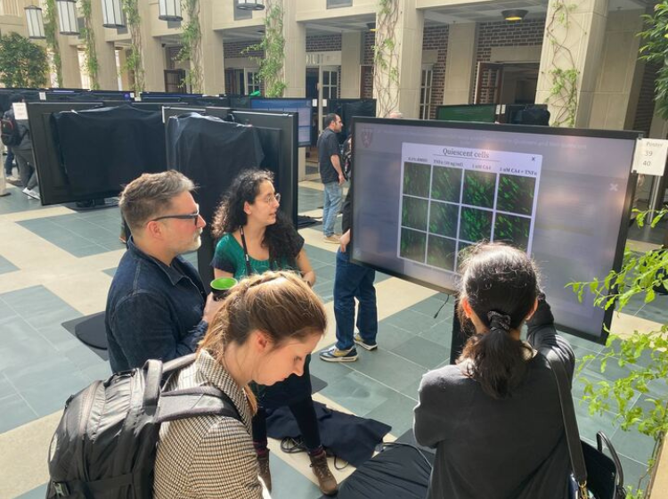 4 people standing in front of and looking at an iPoster screen at the HHMI March science meeting. 