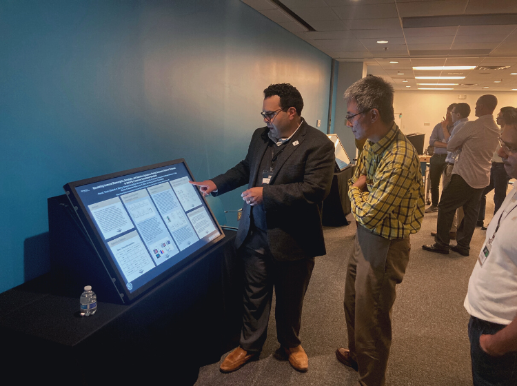 Person presenting an iPoster on a big screen at the V Scholar Summit 2022, while another person watches on