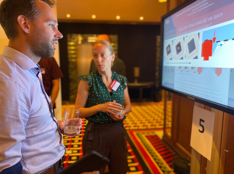 side view of a person looking at a large screen with an iPoster on it. Behind them in the center of the shot is another person facing the camera but looking at the first person. 