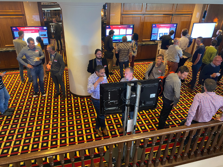 Crowd of people at Thermo Fisher MSD technology conference 2022. They are networking and talking together in smaller groups. Some individuals are reading iPosters displayed  on standing screens.