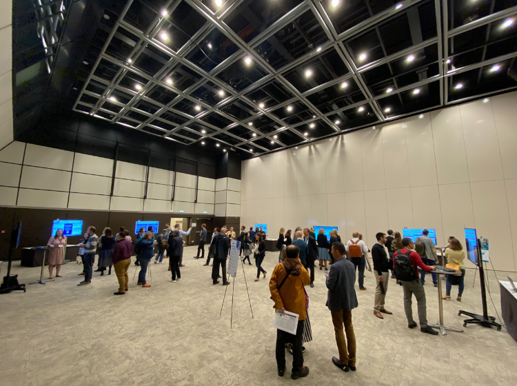 A crowd of people at the in the iPoster hall at the ISOQOL Annual meeting. They are gathered around the iPoster screens in smaller groups. 