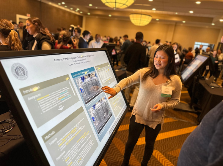 Person at K-INBRE Symposium standing in front of and touching a large angled screen with an iPoster on it. 