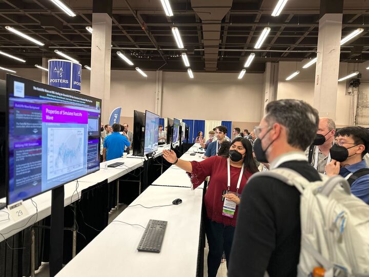 A presenter showcasing their research on an iPoster at AAS 242. Two attendees are standing next to the presenter and looking at the screen. 