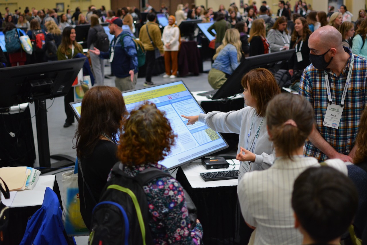 Crowd's of attendees interactiing with author/presenters at ASHA ELEVATE Convention 2024. Focused on one presenter pointing at their presentation screen.