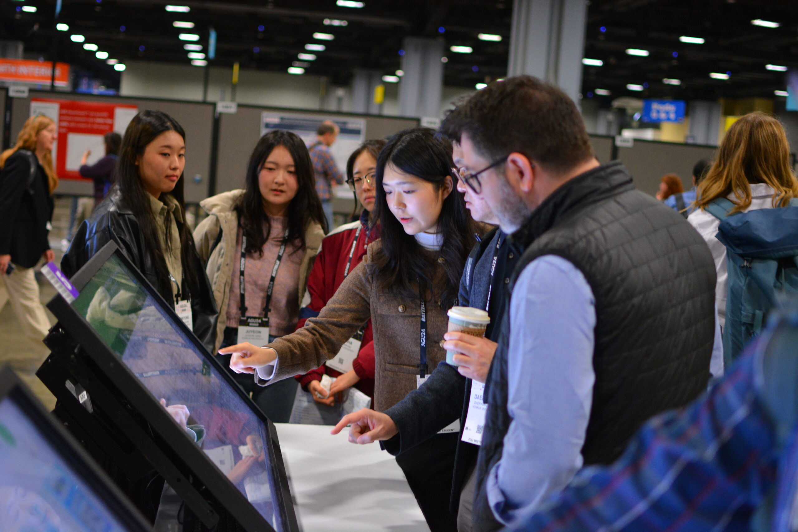 A group of 6 people studying the content on a touch screen ath the AGU 2024 Fall meeting. The AGU meeting theme is What's next for Science?