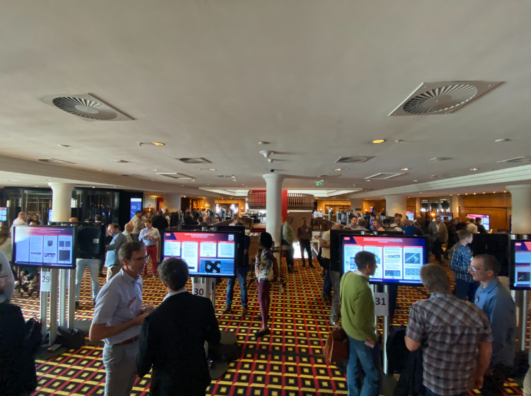 Crowd of people at Thermo Fisher MSD technology conference 2022. They are networking and talking together in smaller groups. Some individuals are reading iPosters displayed  on standing screens.