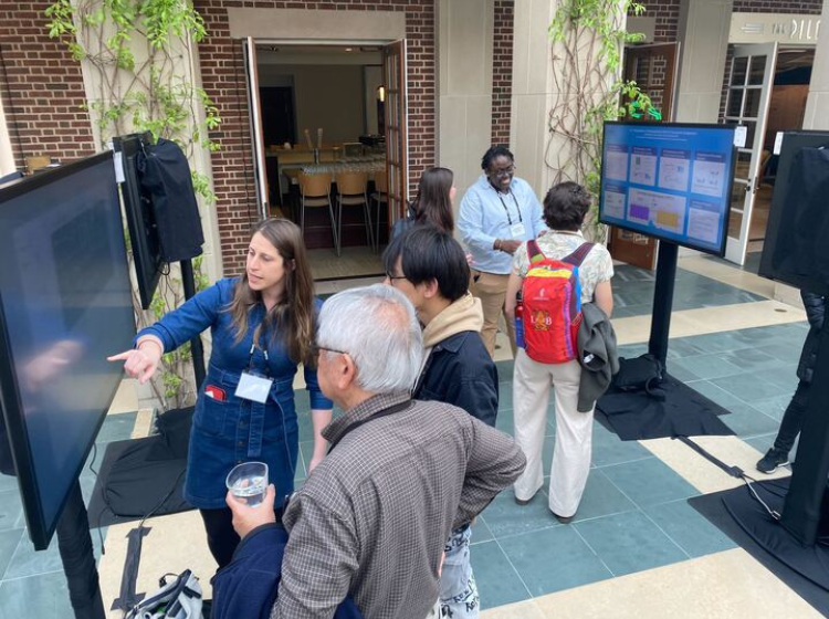2 groups of people standing around 2 separate iPoster screens during a poster session at the HHMI March Science Meeting.
