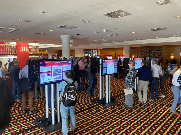 Crowd of people at Thermo Fisher MSD technology conference 2022. They are networking and talking together in smaller groups. Some individuals are reading iPosters displayed  on standing screens.