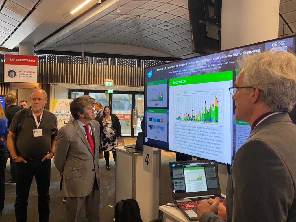 A person presenting an iPoster on a large screen at GLOC 2023. while another person stands opposite them and looks at the screen.