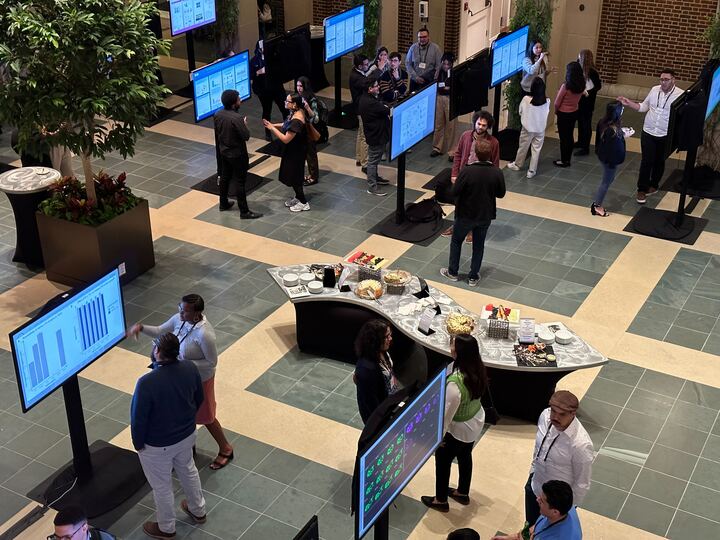 IPoster session in progress at The HHMI Annual Gilliam Meeting. A room full of standing screens with people milling around them and interacting with one another. 