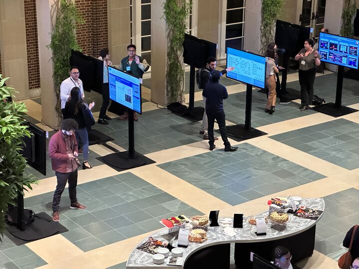 IPoster session in progress at The HHMI Annual Gilliam Meeting. A room full of standing screens with people milling around them and interacting with one another.