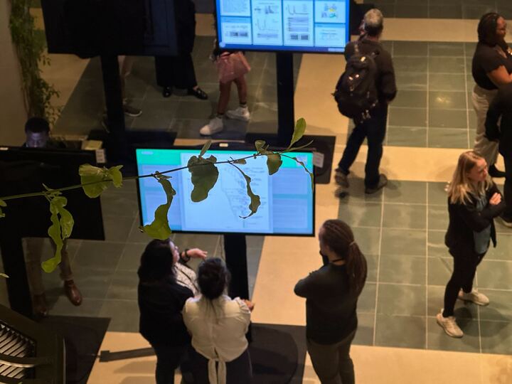IPoster session in progress at The HHMI Annual Gilliam Meeting. 3 people standing around a screen with an iPoster on it.