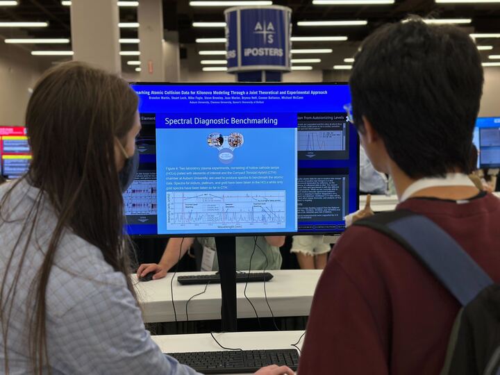 Two people facing an iPoster on a large standing screen at AAS 242. 